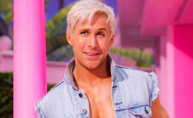 A man with blond hair in a denim vest smiles in a colorful, vibrant setting.