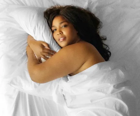 Person comfortably lying on a white silk pillowcase and sheets, showcasing luxury bedding.