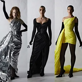 Three models in metallic silver, black, and yellow gowns with long gloves, posing against a plain background.