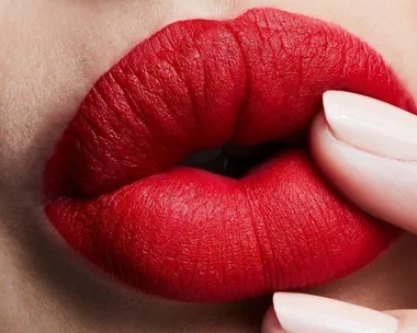 Close-up of vibrant red lipstick on lips with fingers lightly touching.