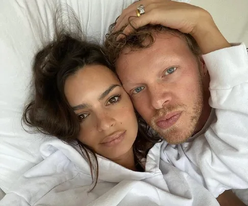 A woman and a man lying together, both wearing white, with the man's head resting on the woman's and their faces close.