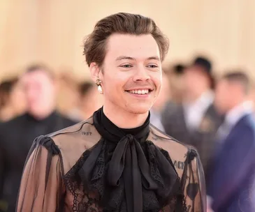 A person smiling, wearing a sheer black outfit with intricate lace details, at a formal event.