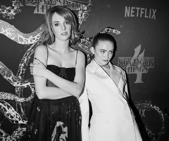 Two individuals in formal attire at a "Stranger Things 4" event, posing in front of a themed backdrop.