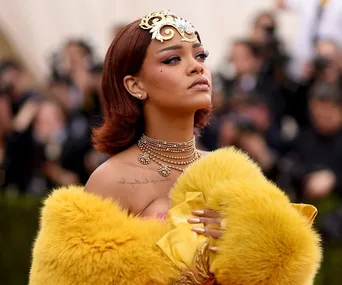 Rihanna wearing an ornate headpiece, luxurious jewelry, and a yellow fur-trimmed outfit at a formal event.