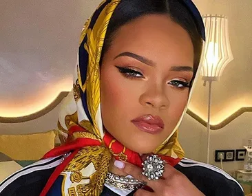 Rihanna wearing a patterned scarf and ornate ring with dramatic makeup in a stylish indoor setting.