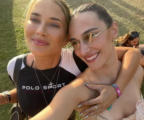 Two women smiling and embracing outdoors, with one wearing a Polo Sport shirt and the other with sunglasses, on a sunny day.