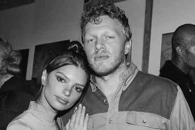 A black-and-white photo of a woman and a man posing closely, with blurred people in the background.