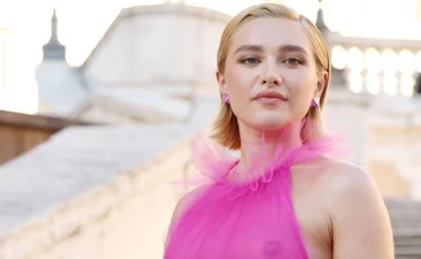 Person wearing a sheer pink gown stands outdoors with a confident expression.