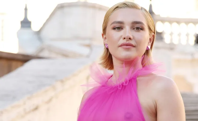 Person wearing a sheer pink gown stands outdoors with a confident expression.
