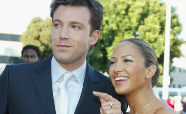 A couple smiling together outdoors, the woman pointing and wearing elegant jewelry.