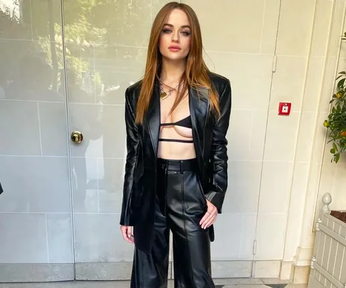 Person in a stylish black leather outfit with a cropped top, posed against a light-colored wall.