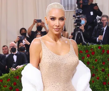 Kim Kardashian at the Met Gala in a sparkling dress, posing on a red carpet with photographers in the background.