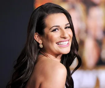 Smiling woman with long dark hair, wearing earrings, looking over her shoulder at an event.