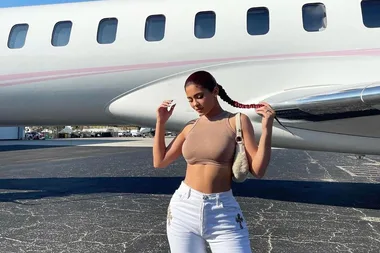 Woman in crop top and white pants posing confidently next to a private jet on an airstrip.