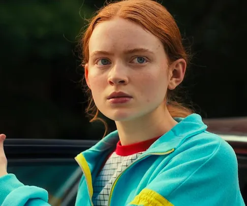 Young girl with red hair in a teal zip-up jacket looking serious, from Stranger Things Season 4.