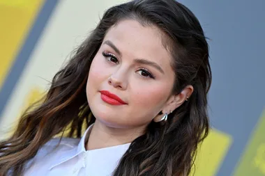 A woman with long brown hair, red lipstick, and wearing a white shirt at a public event.