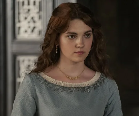 Young woman in a light blue medieval-style dress with long wavy hair, looking determined, from "House of the Dragon."