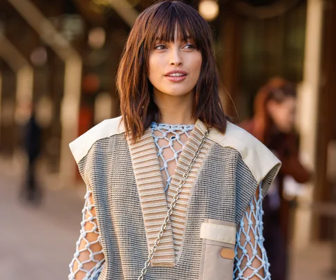 Person in a stylish outfit with a netted top and short brown hair, standing outdoors.