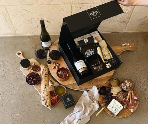 A luxury hamper with wine, snacks, bread, olives, and cheese on a table with cutting boards.