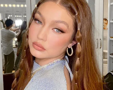 Woman with styled long hair and hoop earrings in a well-lit room with mirrors and vanity.