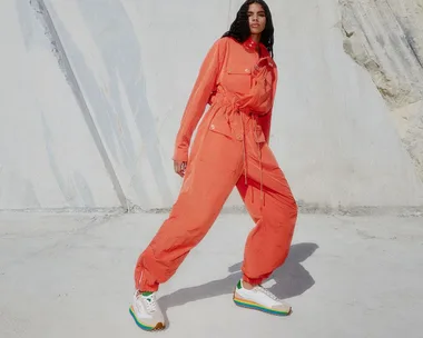 Person in an orange jumpsuit poses against a textured wall, wearing colorful sneakers.