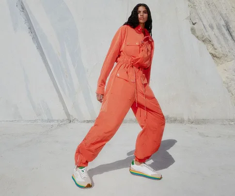 Person in an orange jumpsuit poses against a textured wall, wearing colorful sneakers.