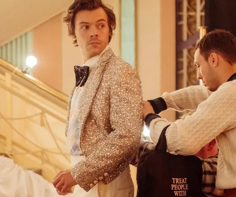 Man in a sparkly suit being assisted by another person, preparing backstage.