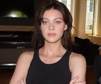 Woman in a black tank top with folded arms, standing in a well-lit room.