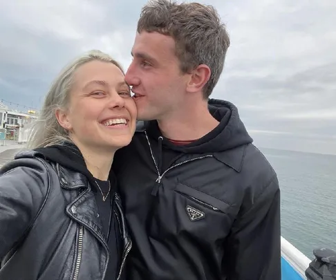 A smiling couple embraces by the ocean on a cloudy day.