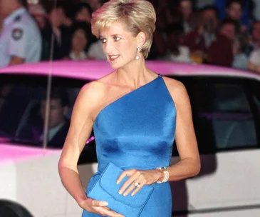 Woman in elegant blue one-shoulder dress holding a matching clutch at a formal event.