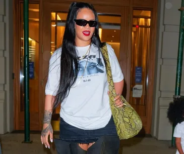 Rihanna in sunglasses, graphic tee, and thigh-high boots, carrying a green snakeskin bag outside a building.