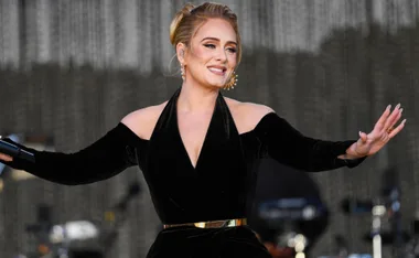 Singer performing on stage in a black dress, smiling with arms outstretched.