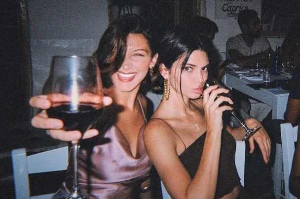 Two women smiling, holding drinks in a dimly lit restaurant setting.