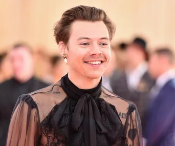 A person wearing a sheer black top with lace and a pearl earring, smiling at a formal event.