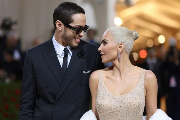 Man in black suit and woman in embellished nude gown looking at each other on a red carpet event.