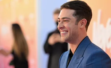 Smiling man in a blue suit at an event with a colorful blurred background.