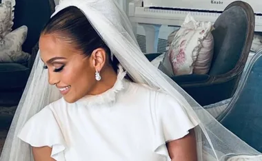 Bride in elegant wedding dress and veil sits smiling, with floral pillows in the background.