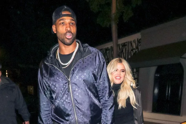 Man in a dark jacket and cap walking with a smiling woman with long blonde hair at night.