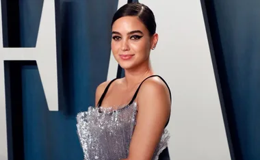 Woman in a glittery silver dress poses at a formal event with a large letter backdrop.