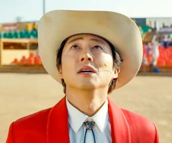 A man in a cowboy hat and red jacket looks up in an outdoor arena.