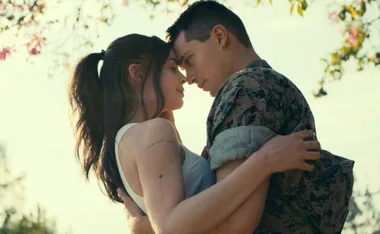 A couple embracing under a tree, the man in a military uniform and the woman with tattoos on her arm.