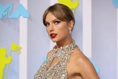 Woman in a sparkling, silver halter dress poses on the MTV VMAs red carpet with a backdrop featuring the MTV logo.