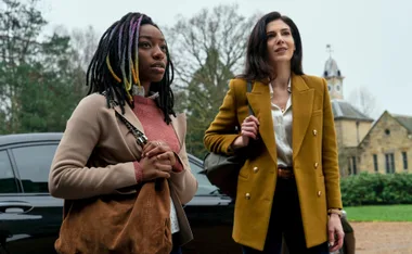 Two women standing outdoors, one with colorful hair, the other in a mustard coat, in a scene from "The Sandman" series.