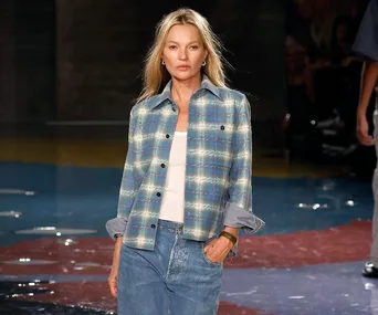 A person walking on a runway wearing a blue plaid shirt and jeans.