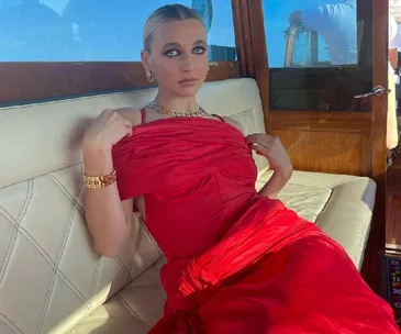 Woman in a red dress sitting on a boat bench at the Venice Film Festival.