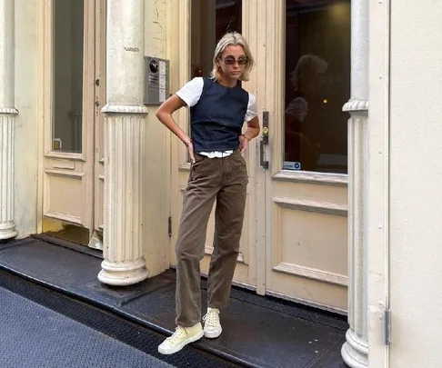 Person in casual outfit with sunglasses, standing confidently outside a building with cream columns and glass doors.