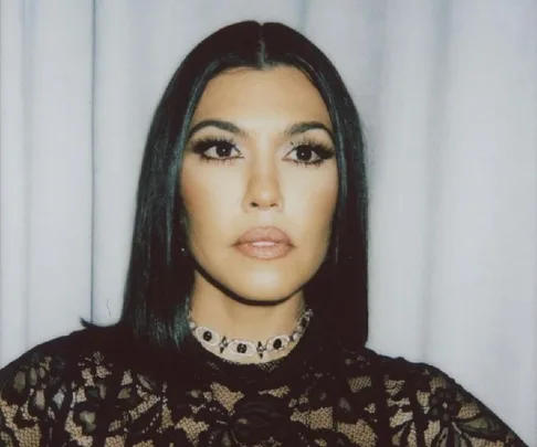 A woman with straight dark hair and a lace floral outfit poses against a light backdrop.