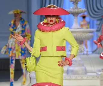 Model in a vibrant green outfit with pink inflatable accessories on the runway at Milan Fashion Week SS23.