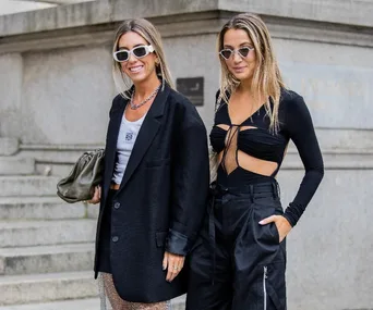 Two women in stylish black outfits pose confidently during London Fashion Week SS23 street style.