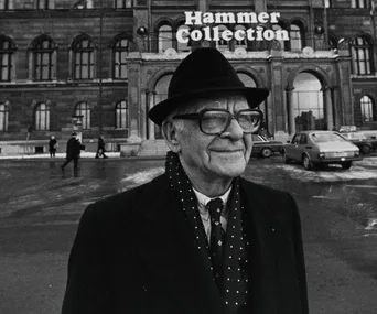 An elderly man in a suit and hat stands outside a building labeled "Hammer Collection" with cars in the background.